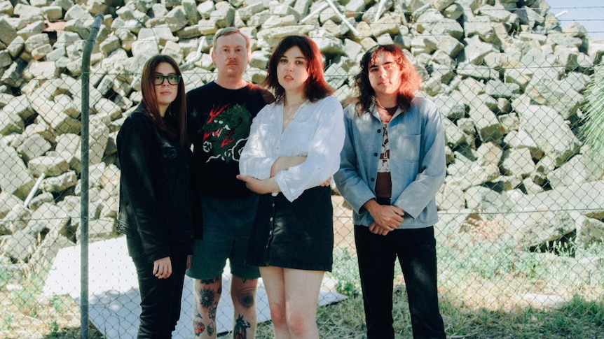 Four members of band RVG stand in front of a fence and big pile of rocks