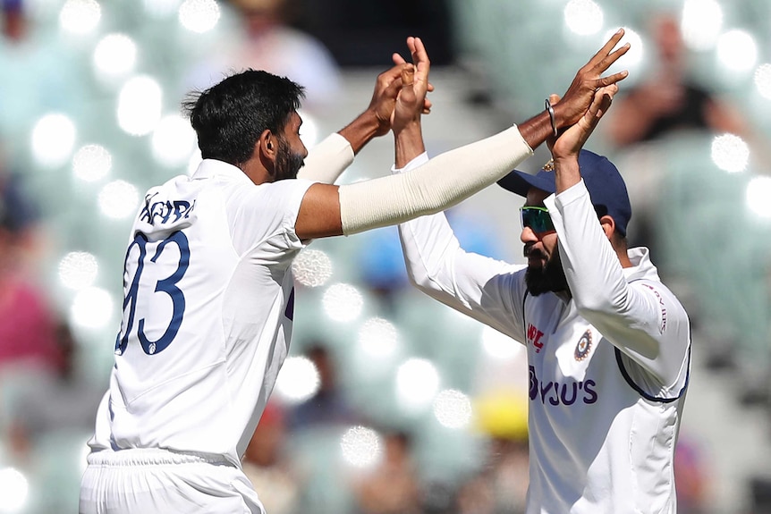 Two Indian cricket players wearing white clothes high five.
