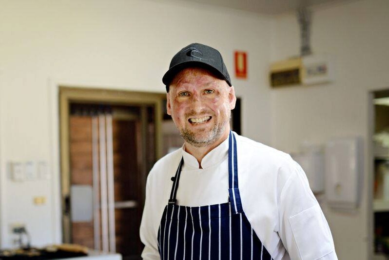 A chef stands smiling in a kitchen.