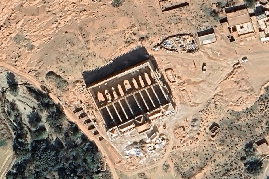 A birds eye view shows a historic stone building in a dusty mountainous landscape