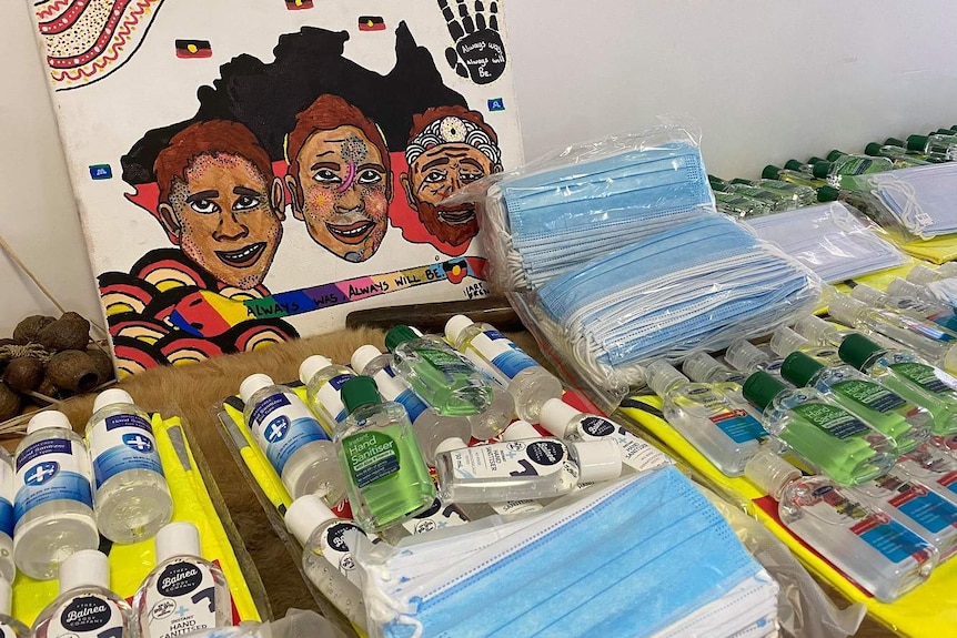 Hand sanitisers and face masks lined up on the bench in front of an Aboriginal painting.
