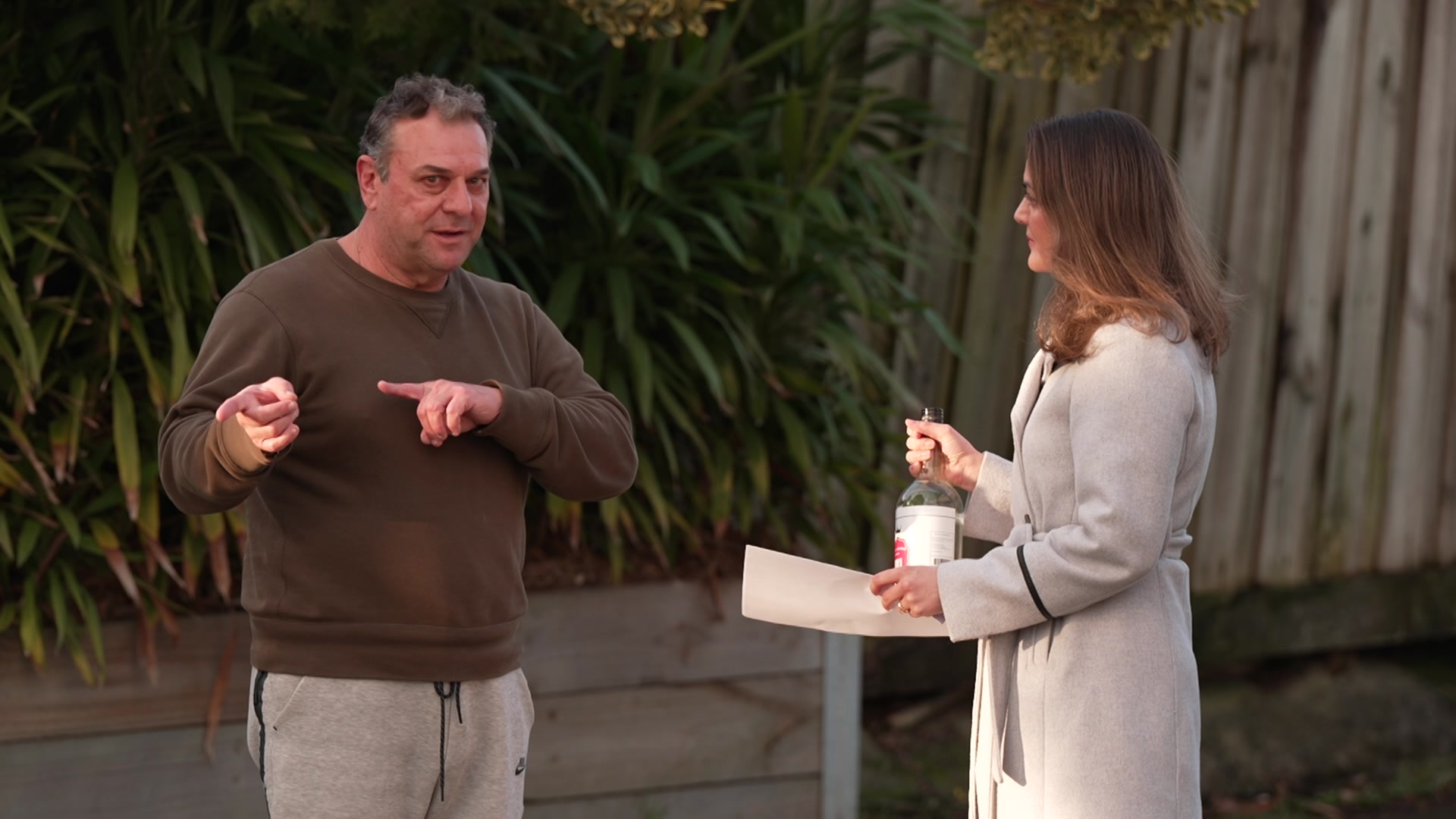 A reporter holding a bottle of vodka speaking to a man.
