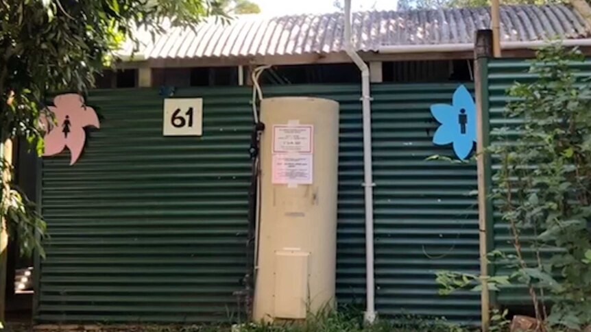 A corrugated iron toilet block framed by trees with women's and men's signs and a hot water cylinder