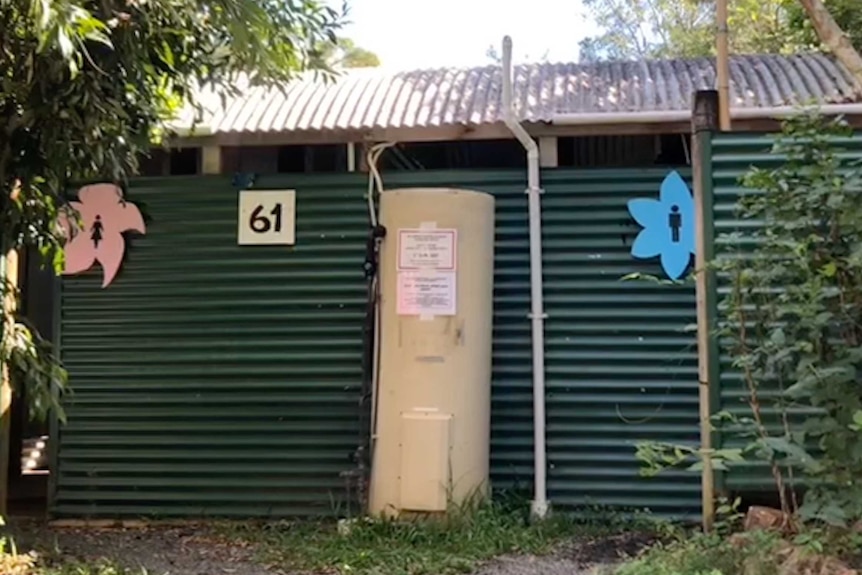 A corrugated iron toilet block framed by trees with women's and men's signs and a hot water cylinder