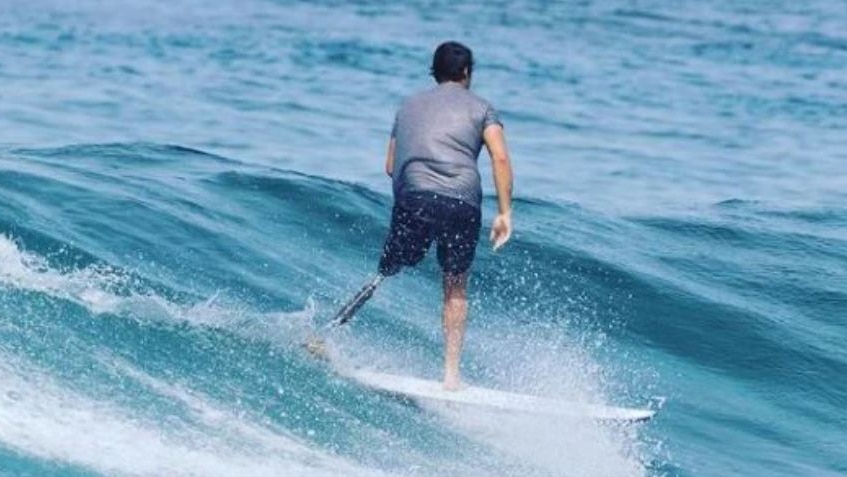 A young man with a prosthetic left leg on a surf board