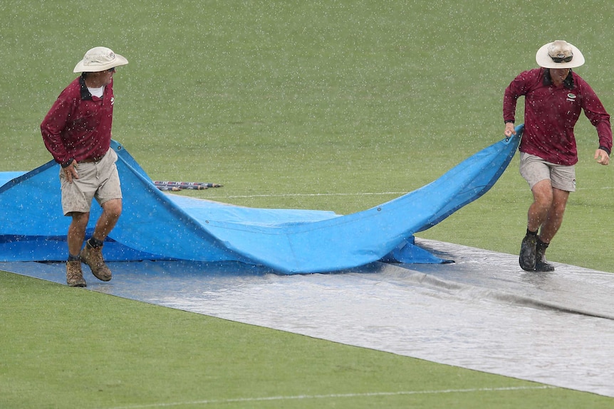 Ground staff bring the covers on at the Gabba as rain falls in a Sheffield Shield match in October.