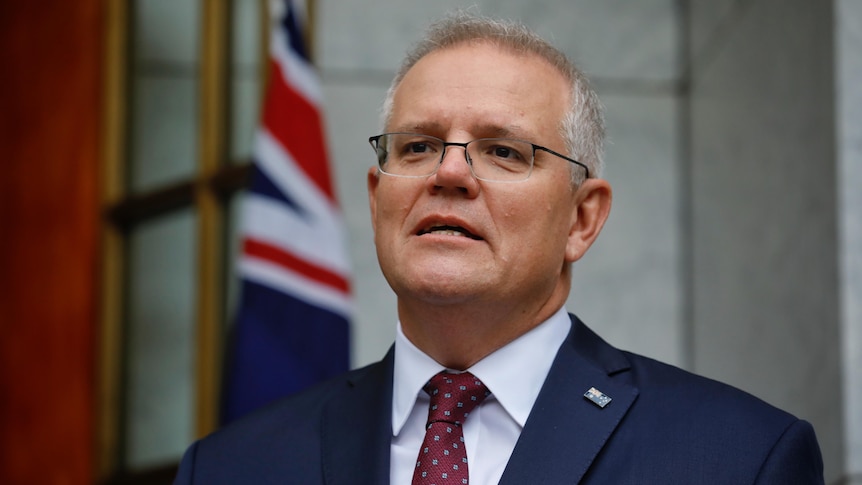 A strained Scott Morrison looks into the distance with an Australian flag behind him