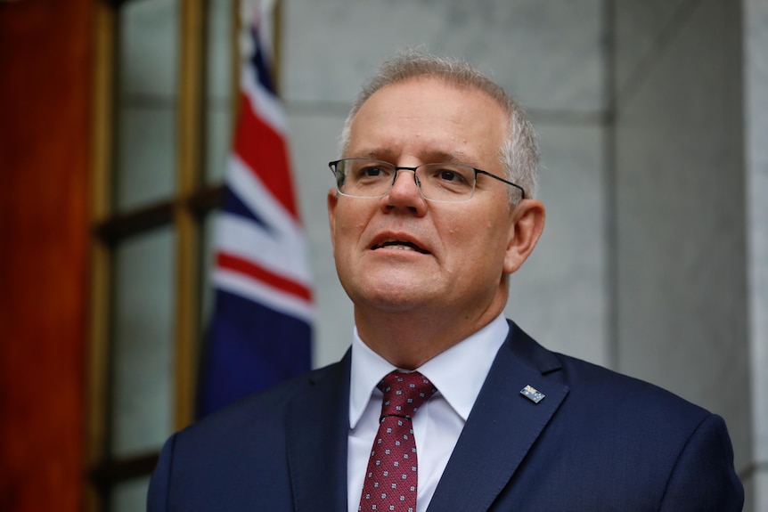 A strained Scott Morrison looks into the distance with an Australian flag behind him