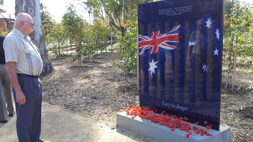 Man stands before war memorial covered in poppies