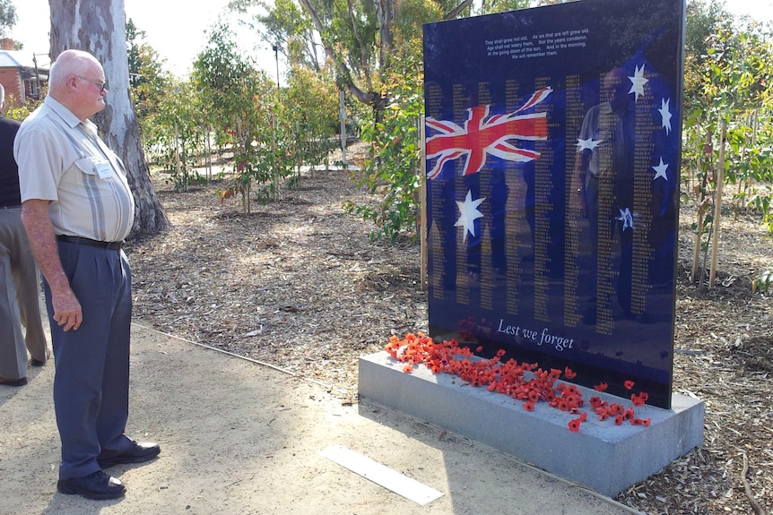 Man stands before war memorial covered in poppies