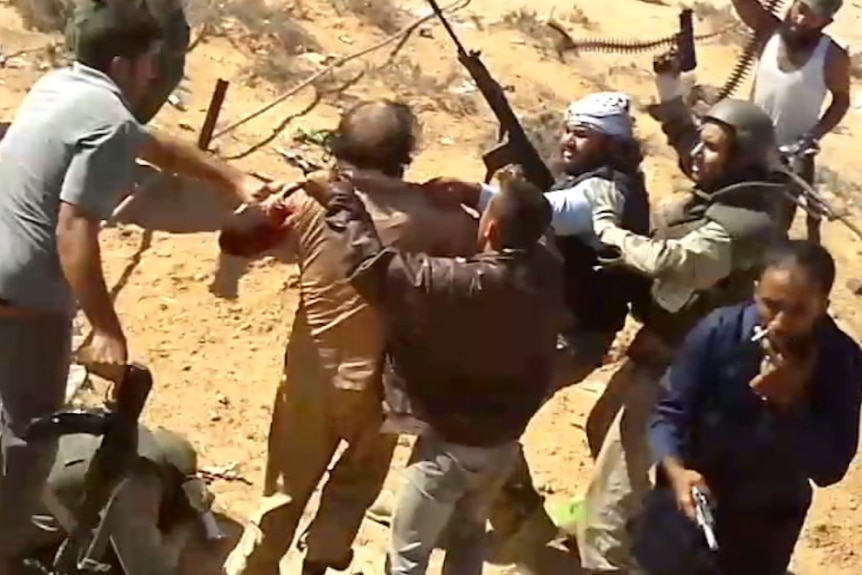 A video still shows Gaddafi held by a group of men with guns.