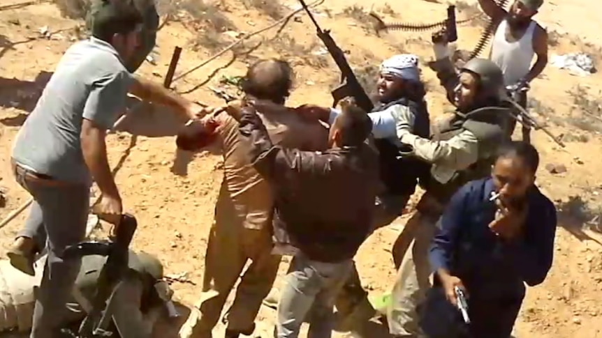A video still shows Gaddafi held by a group of men with guns.