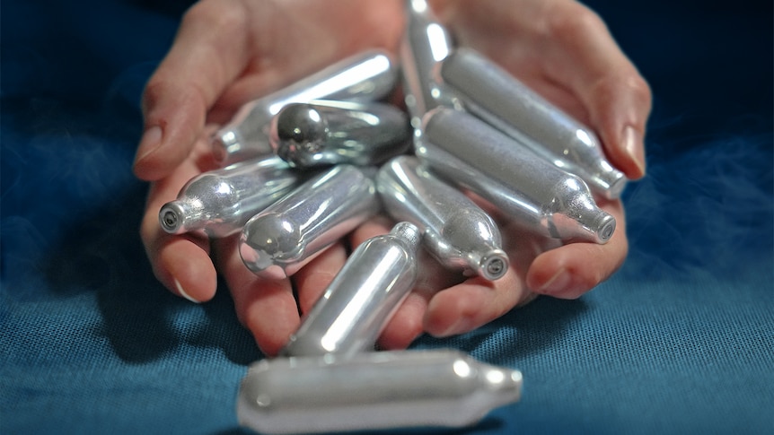 A graphic image of a person holding about 10 nangs, which are small cannisters of nitrous oxide.