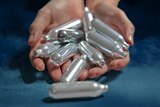 A graphic image of a person holding about 10 nangs, which are small cannisters of nitrous oxide.