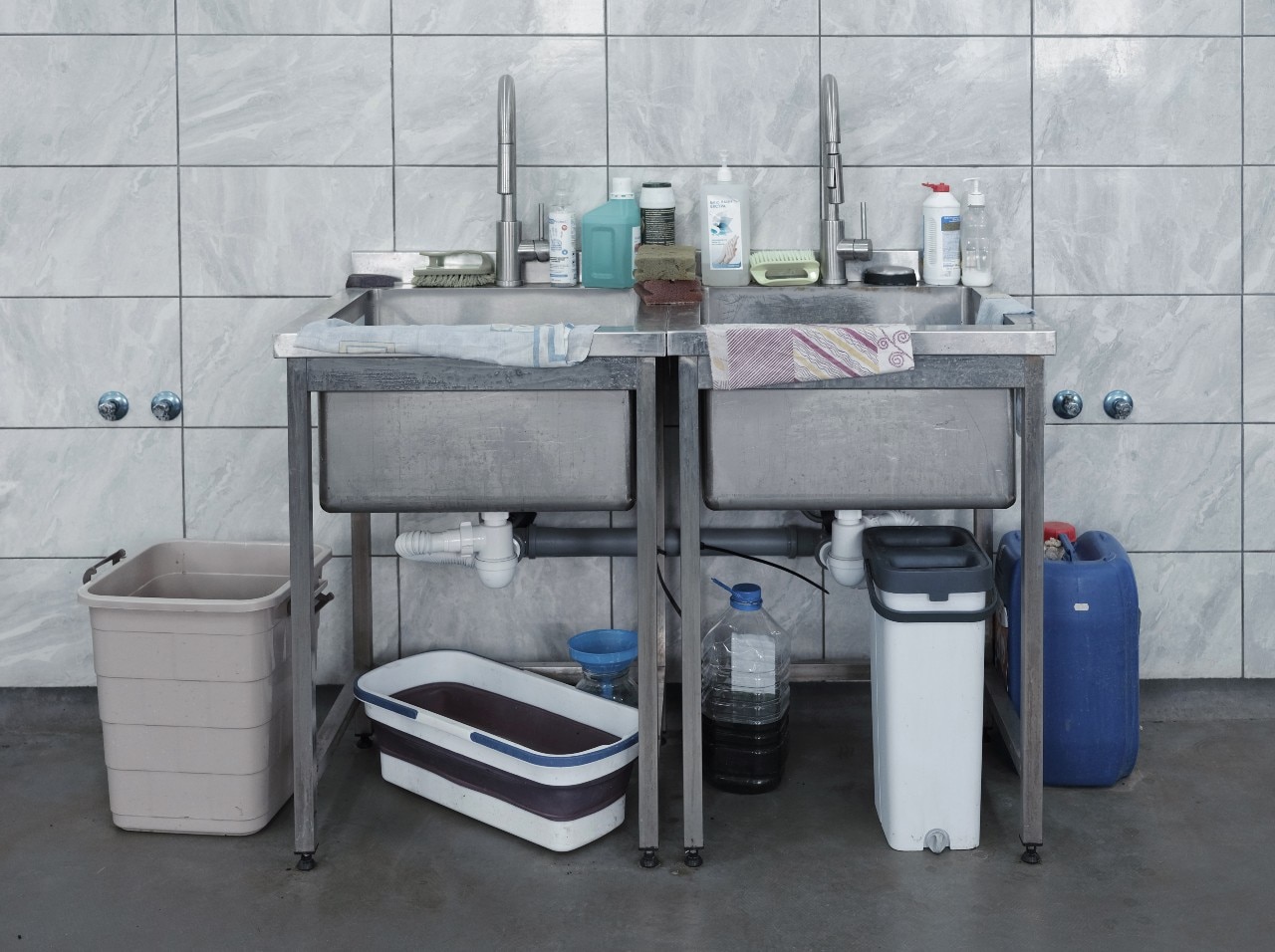Two sinks with several bottles of what appear to be cleaning supplies on top of them.