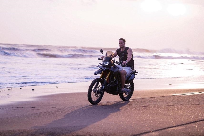 A man rides a motorike along a beach. 