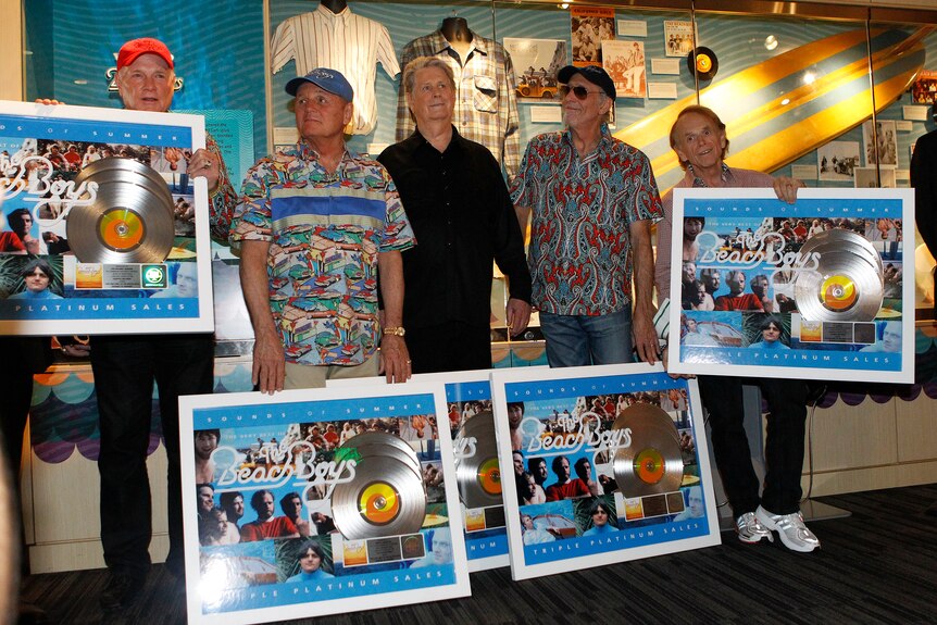 Five men stand holding silver records in frames.