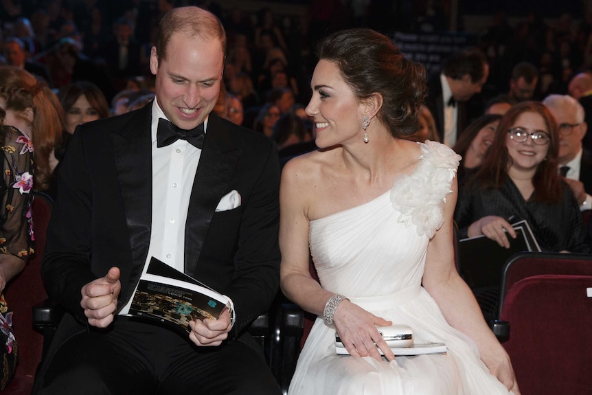 Prince William, left, wears black tuxedo with white shirt and black tie, with Kate sat next to him in white one-shoulder gown.