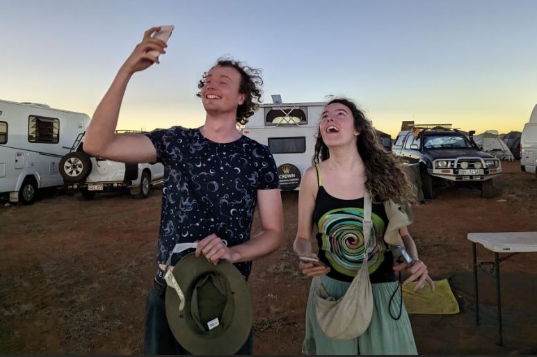 Two happy looking people look to the sky at a campsite.