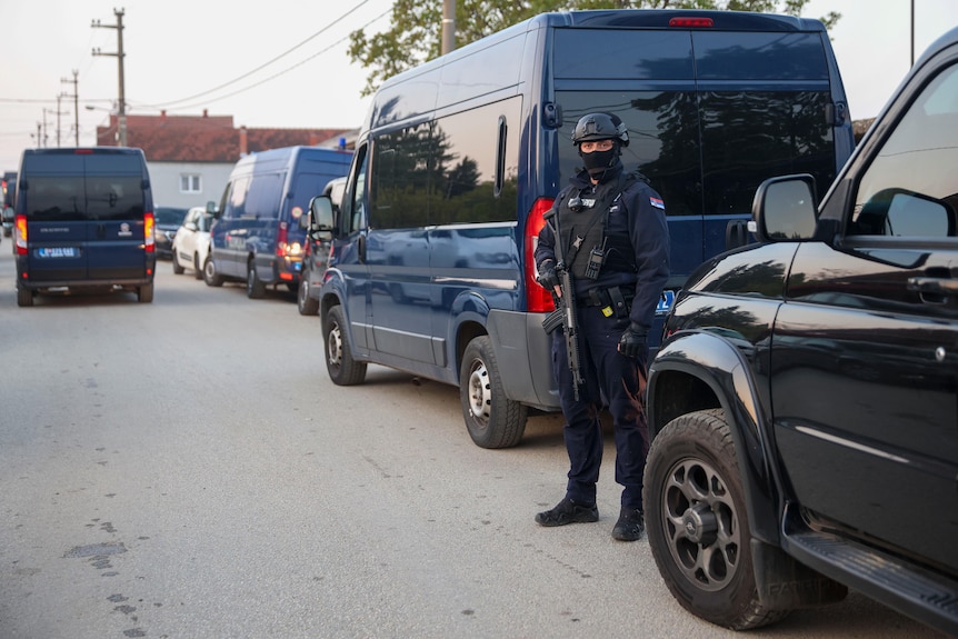 A police officer stands guard near a van and other cars following a shooting in Dubona, Serbia