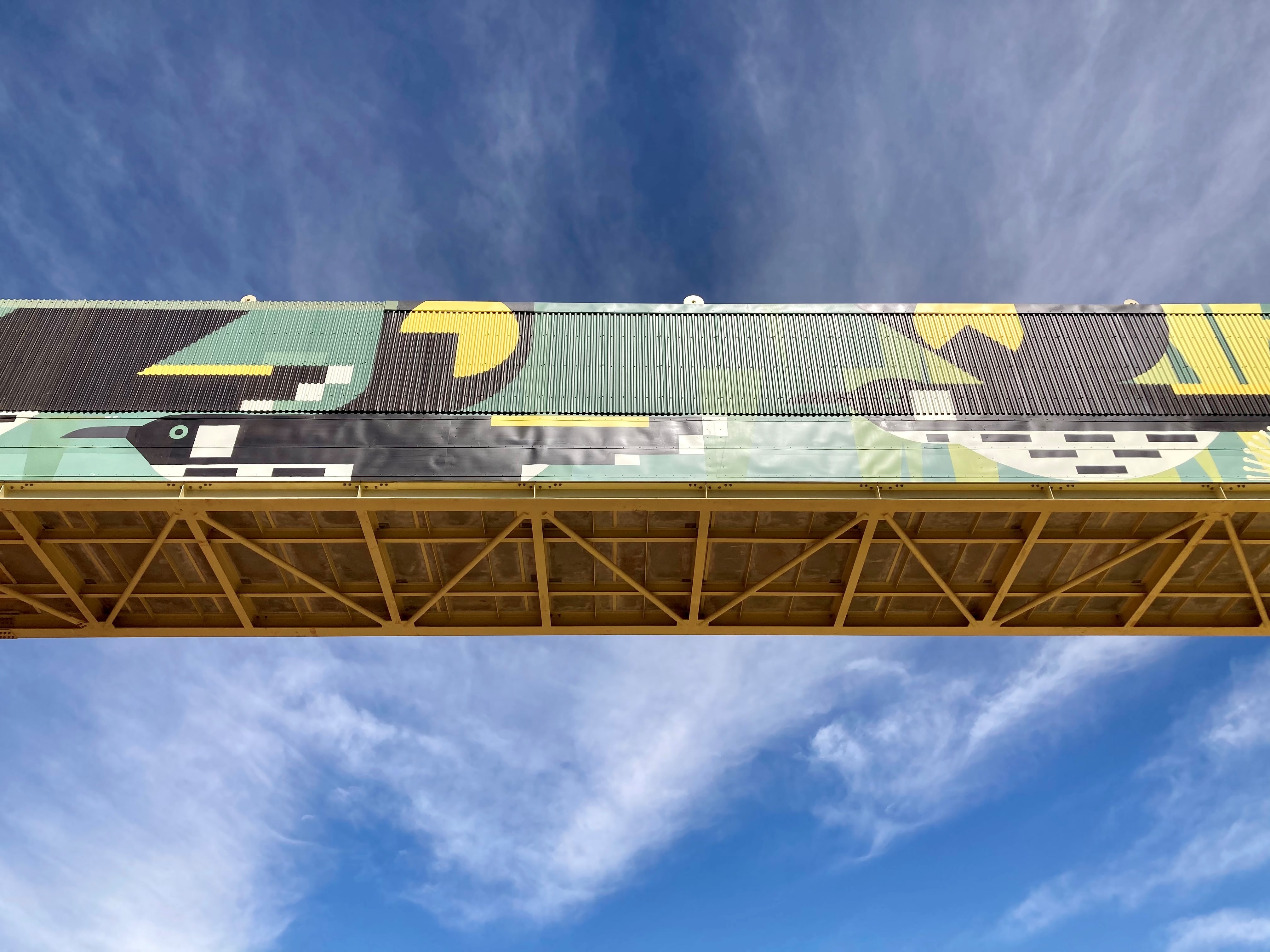 Mine over pass from underneath with a bright green and black mural on it - in front of a clear blue sky