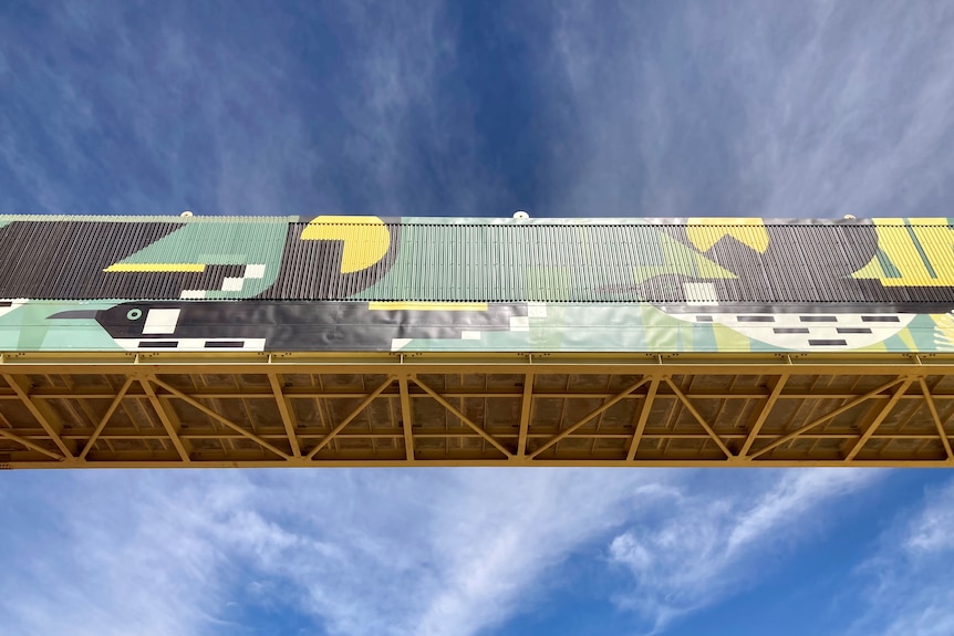 Mine over pass from underneath with a bright green and black mural on it - in front of a clear blue sky
