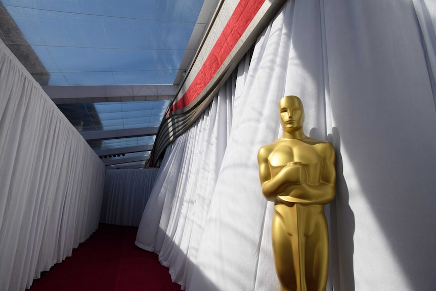 A large Oscars statue sits in front of a hallway made of curtains.