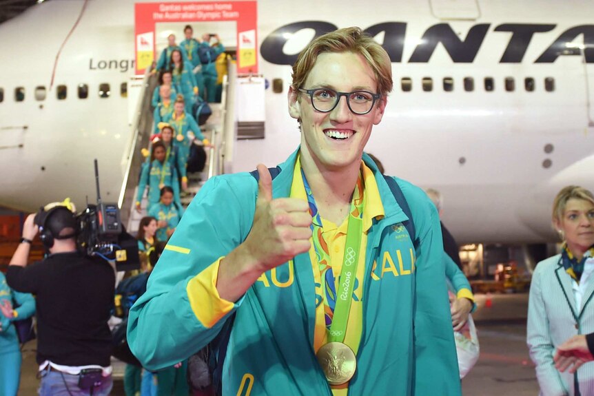 Swimming Mack Horton gives a thumbs up symbol in front of a plane