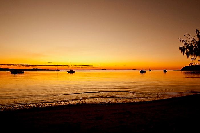 Sunset on beach with boats in ocean.