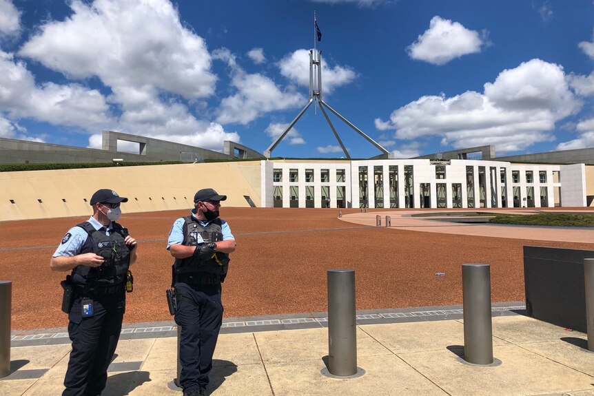 Two uniformed police officers stand outside parliament house.