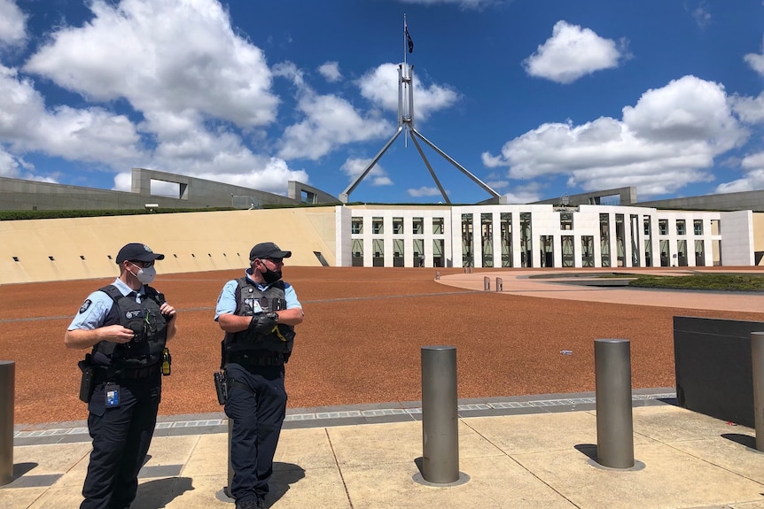 Two uniformed police officers stand outside parliament house.
