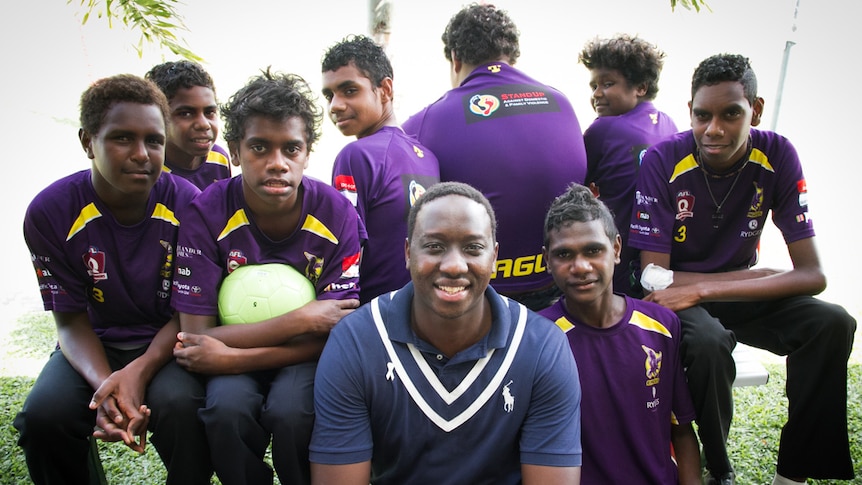 An Aboriginal man sitting in the centre of a group of Aboriginal boys wearing purple shirts.
