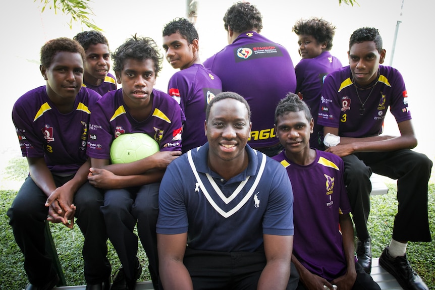 An Aboriginal man sitting in the centre of a group of Aboriginal boys wearing purple shirts.