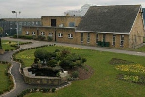 A brick building with a grey roof sits behind a lawn with paths crossing it