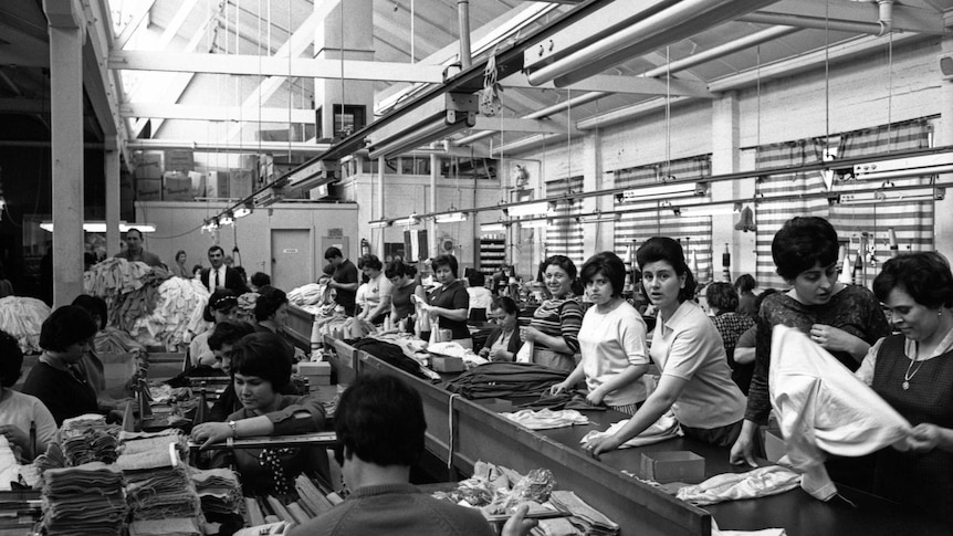 black and white image of female workers in a large industrial space, sorting and folding fabrics