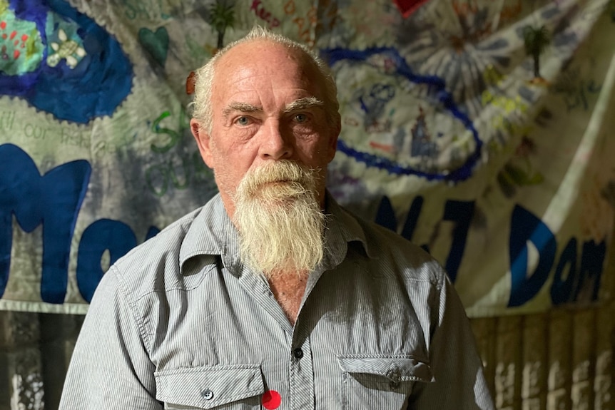 Gavin Finch looks at the camera with a straight face, beard, banner behind.