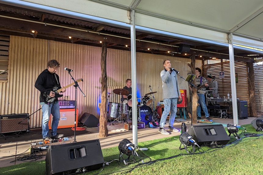 Four men standing under a shade playing instruments and singing