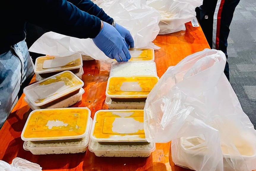 Rice and curry boxes are laid out on a table as somebody wearing blue gloves prepares more