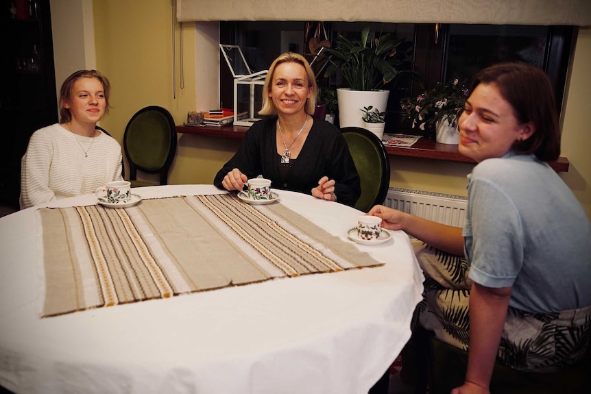 A mother and her two teenage daughters sit around the household table.