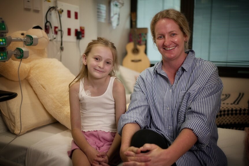 young girl sits next to her mum on the hospital bed