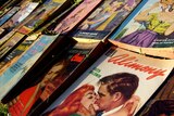 a stack of romance novels with the front book showing artwork of a woman and man kissing. 