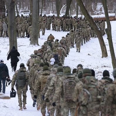 Hundreds of people in military uniform march in the snow