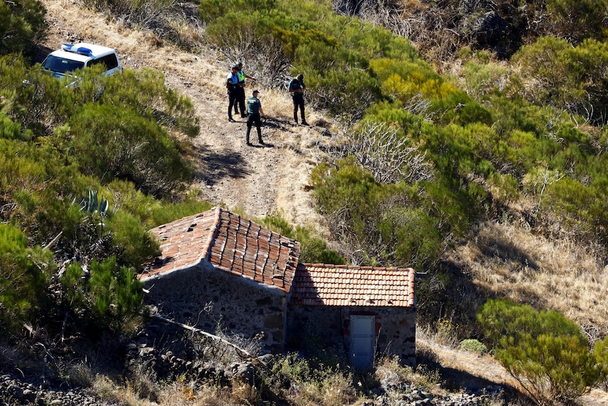 An aerial view of police officers discussing the search near an old farmhouse. 