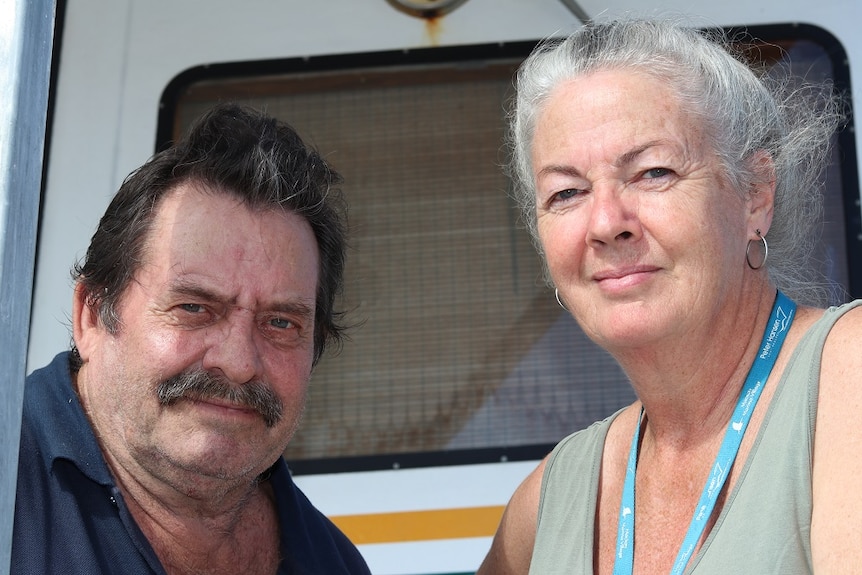 Two people stand on the deck of a boat and look at the camera