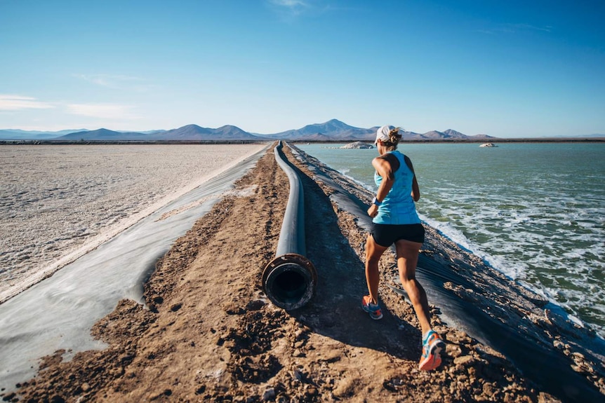 Land on one side and water on the other, a woman runs through the middle next to a large pipe.