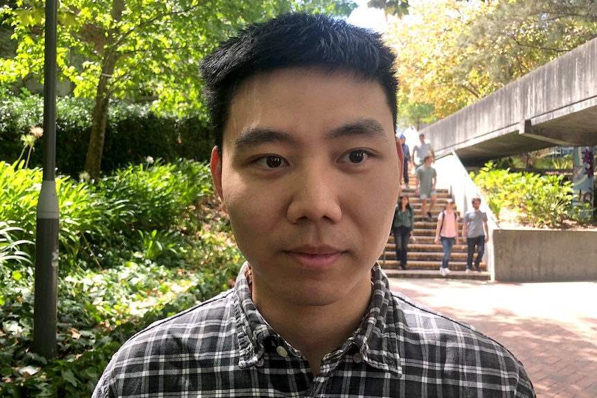 Yao stands on a footpath. A garden and other students are in the background.