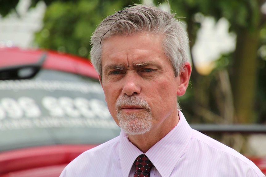 A head and shoulder shot of a middle aged man with grey hair and a goatee wearing a pink striped business shirt and red tie.
