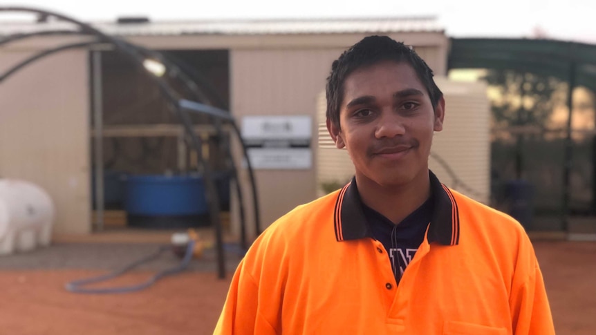teenager wearing orange t shirt outside of the fish farm at remote community Buttah Windee