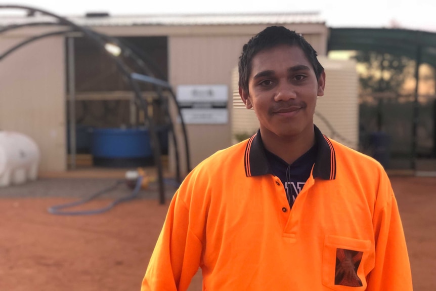 teenager wearing orange t shirt outside of the fish farm at remote community Buttah Windee