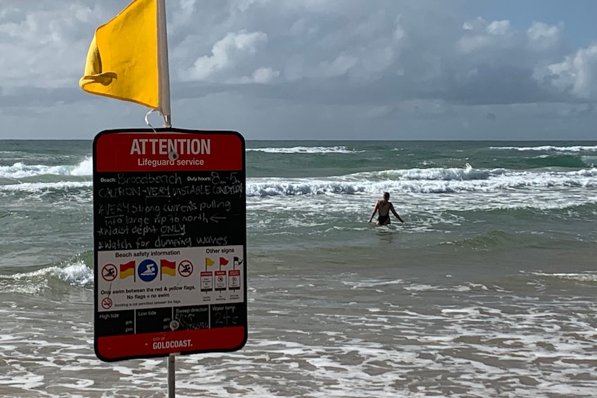 A dangerous beach conditions sign in front of a beach on the Gold Coast with a swimmer entering the water
